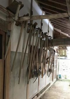 鎌や鍬などの手工具が壁に掛けられている様子